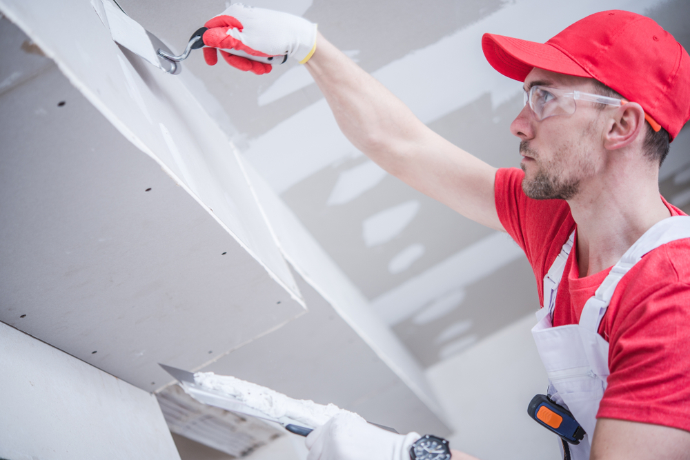 a man wearing overalls and a red shirt working on drywall in a house