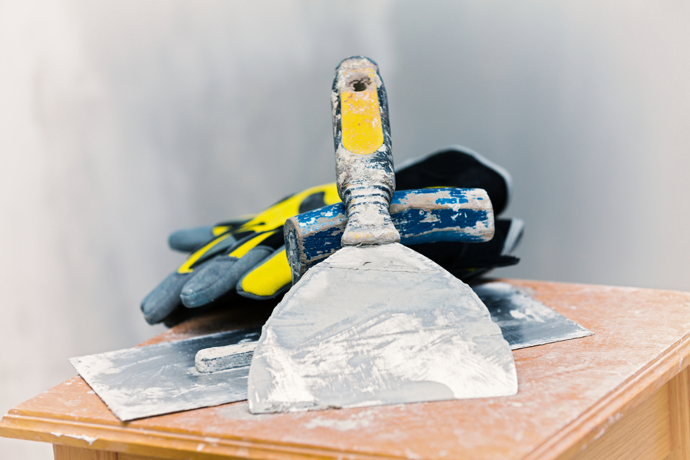 tools used for drywalling, including a pair of gloves and a scraper